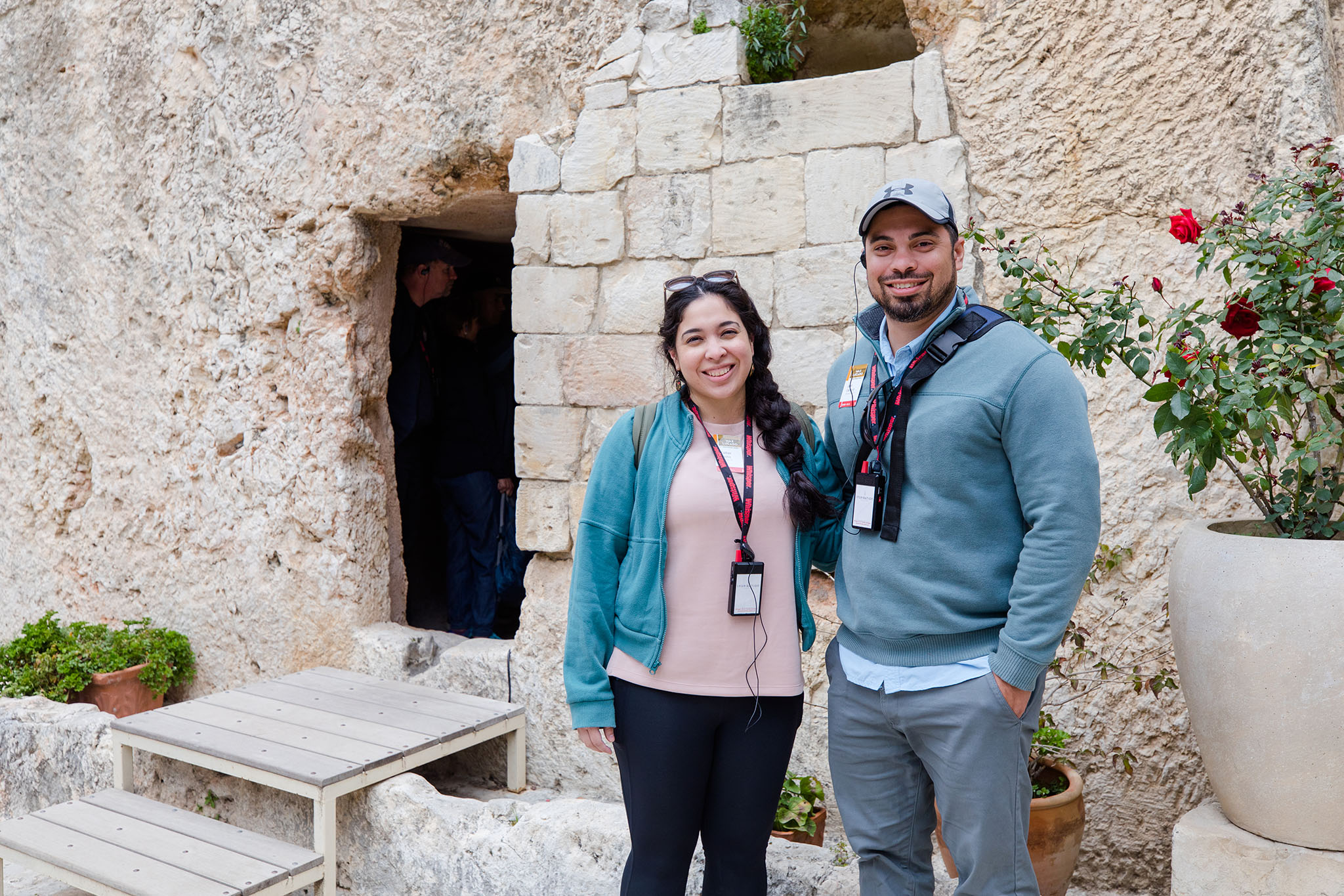 Cheerful couple with lanyards and earpieces posing in front of a historic stone structure.