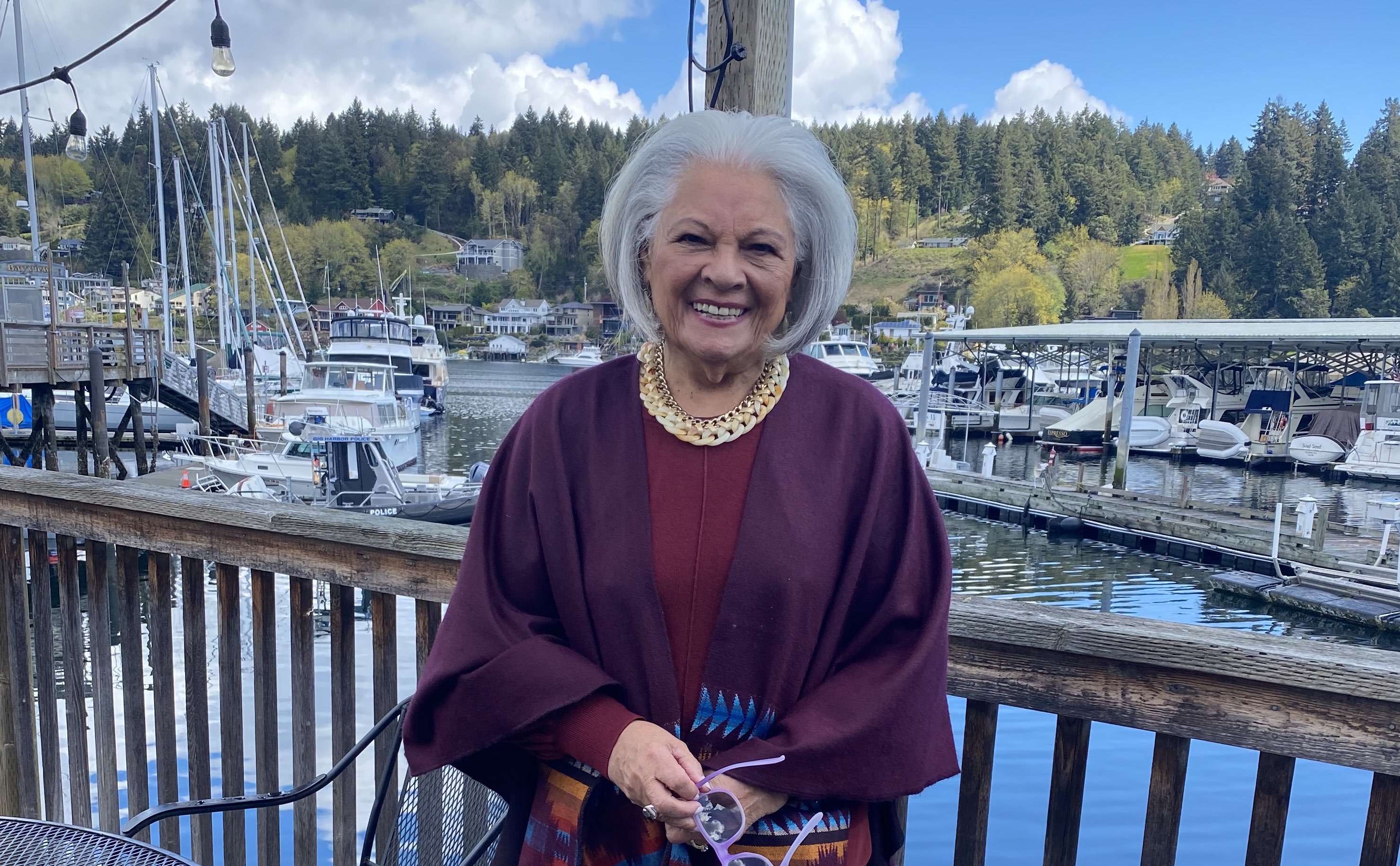 A female traveler standing on a dock, smiles for the camera with boats in the background