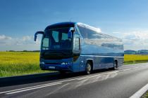 Blue bus driving down a road with green fields in the background