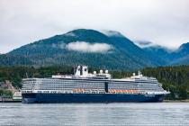 Scenic view of a large cruise ship anchored near a lust forested shortline with foggy mountains in the background.