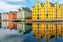 Bright yellow, green, red, and white gabled buildings line the waterfront in Alesund, with their full reflections rippling across the still harbor.