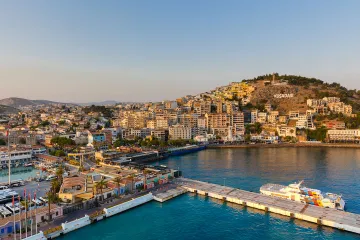 Sunset view of Kusadasi, Turkey, showcasing the vibrant port, bustling cityscape, and the iconic hillside sign.