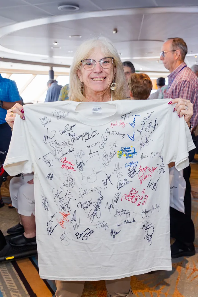 Smiling woman holding up a white t-shirt with numerous signatures on it