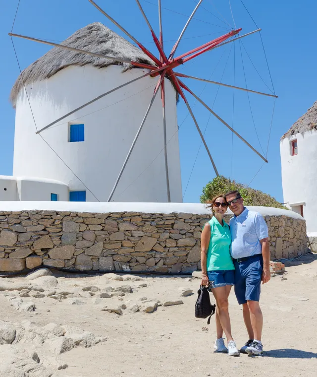 A smiling couple standing together with a large, white windmill behind them